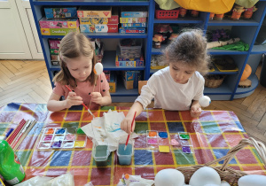 Dwie dziewczynki siedzą przy stole i malują styropianowe jajka