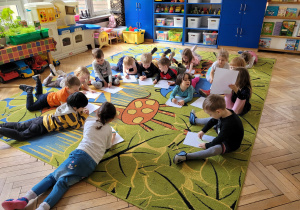 Dzieci leża na dywanie i rysują