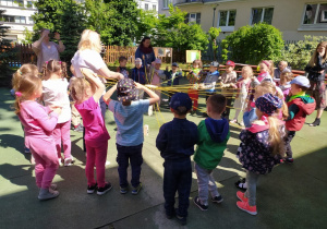 Dzieci na placu zabaw stoja w kole i trzymają żółty sznurek