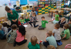 Dzieci ubrane na zielono siedzą na dywanie