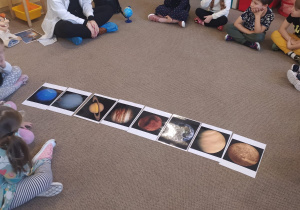 dzieci na dywanie obserwują ilustracje przedstawiające planety