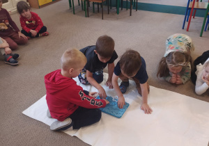 troje dzieci na dywanie obserwuje piasek kinestetyczny