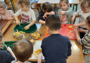 dzieci siedzą przy stoliku i kroją owoce