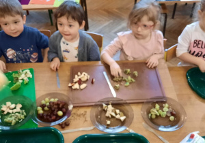 dwie dziewczynki i trzech chłopców przy stoliku kroją owoce