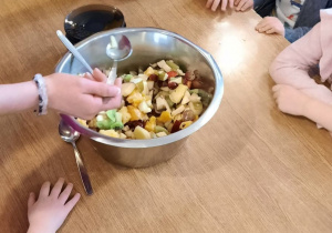 nauczycielka rozdaje dzieciom sałatke na talerzykach